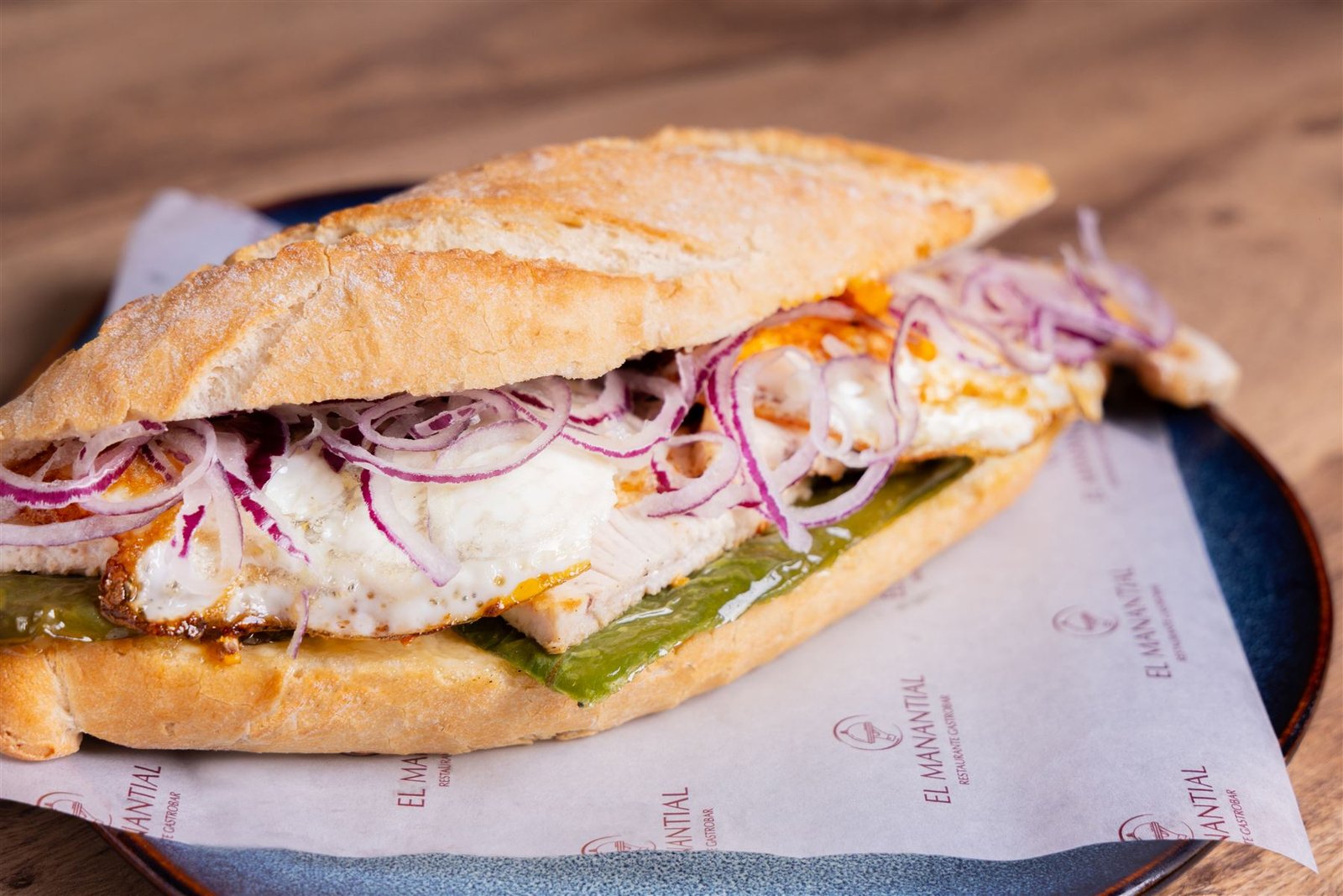 Bocadillo de almuerzo servido sobre papel con el logo del restaurante